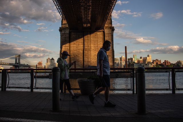 A photo of two people walking near the Manhattan Bridge and Brooklyn Bridge at dusk